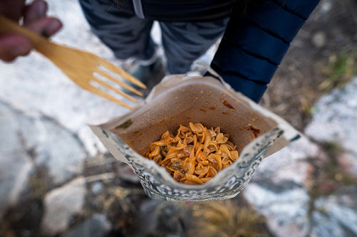 Person in the backcountry enjoying Farm To Summit's Green Chile Mac and Cheese Right out of the bag on the trail